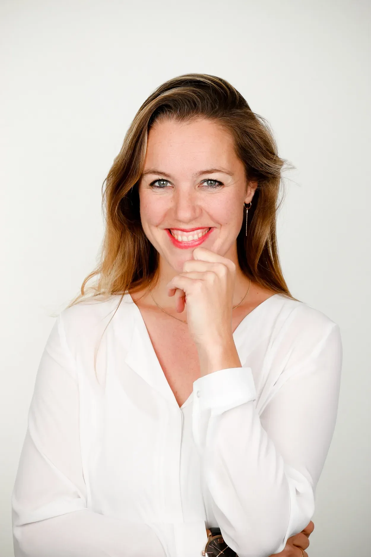 Portret van Alies Tax in een witte blouse, glimlachend met haar hand bij haar kin.